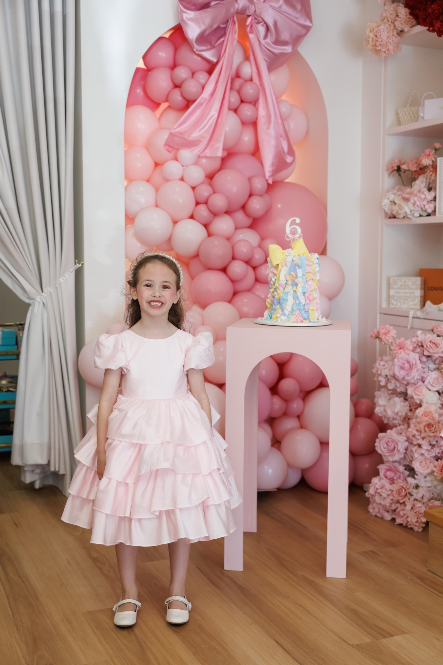 A girl in a party dress in front of a pink balloon wall