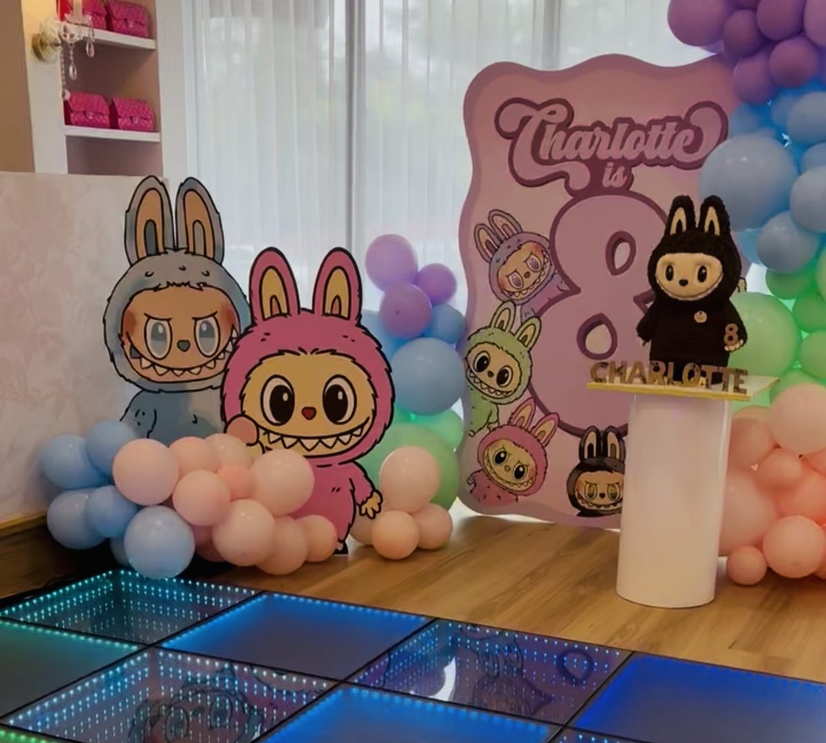 An LED dance floor with balloons and a birthday backdrop at a disco party