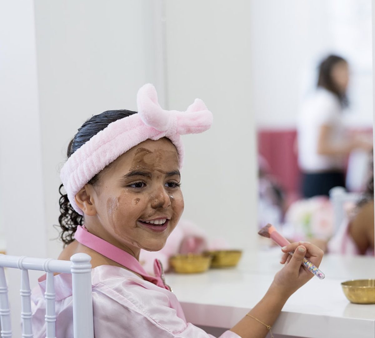 A girl in a pink robe and headband holding a makeup brush at a pamper party