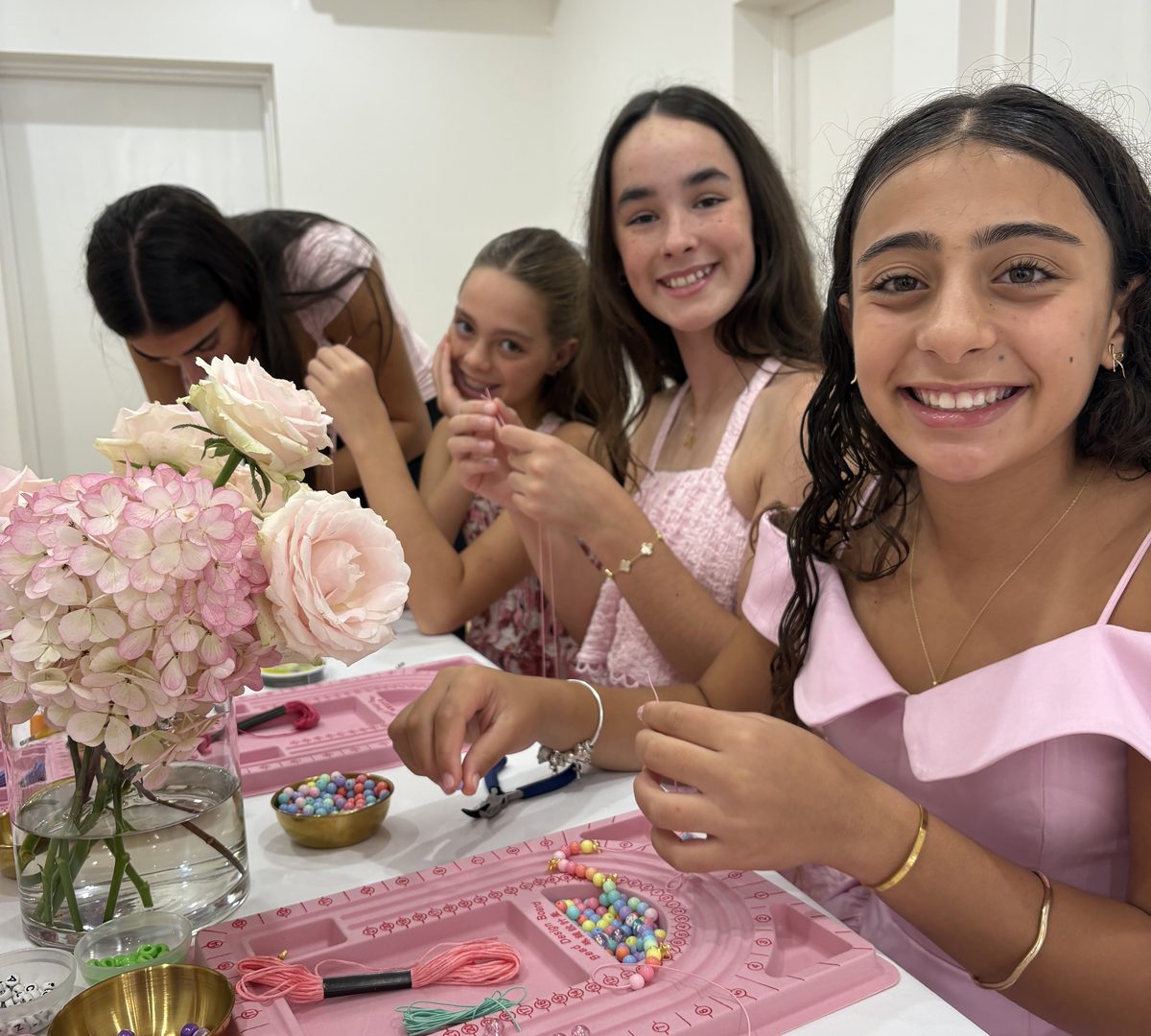 Girls threading beads on a pink bead board at a jewellery making party