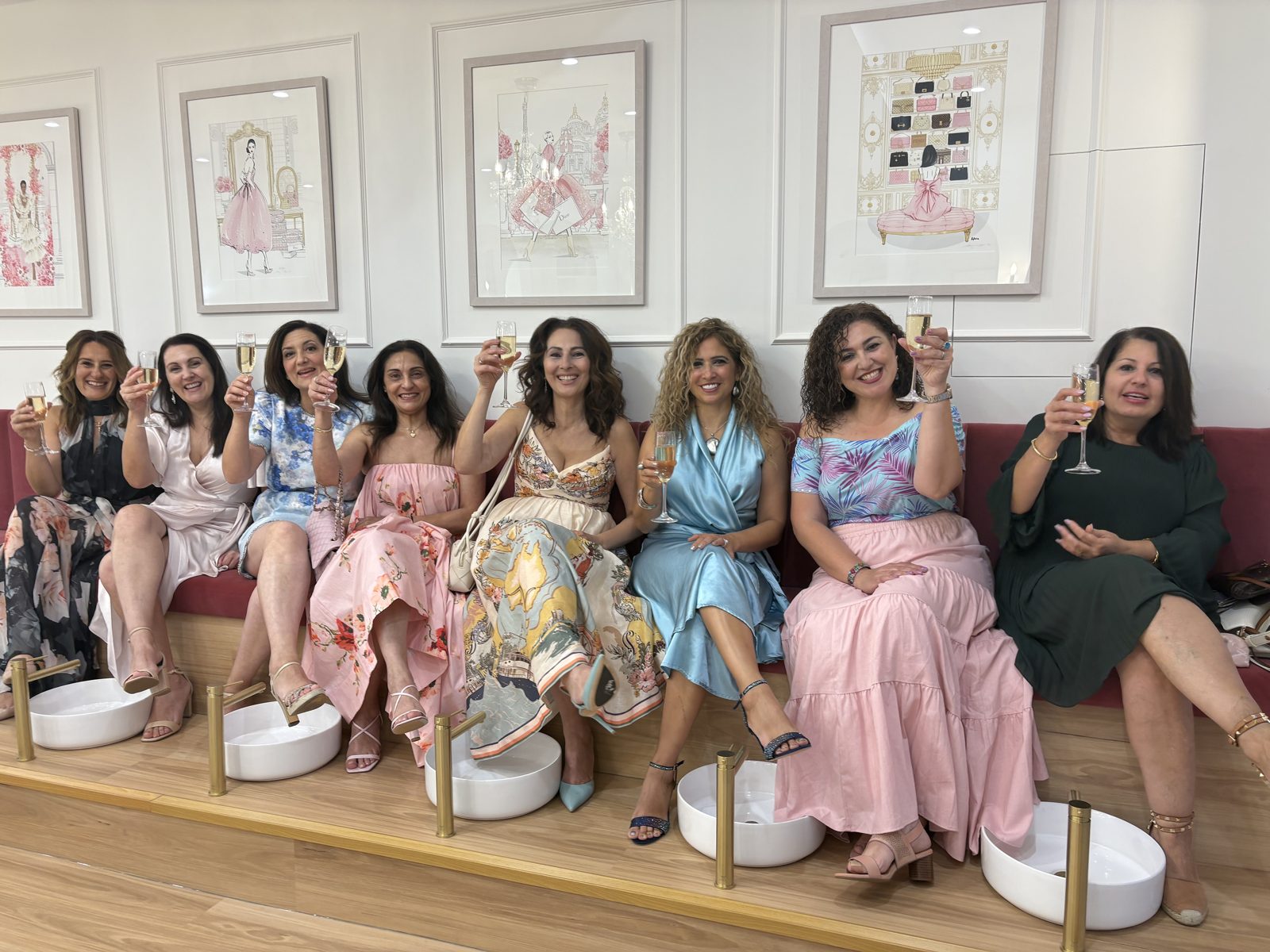 Guests raising champagne glasses with their feet in pedicure bowls at a Belle’s Boutique ladies night pamper party