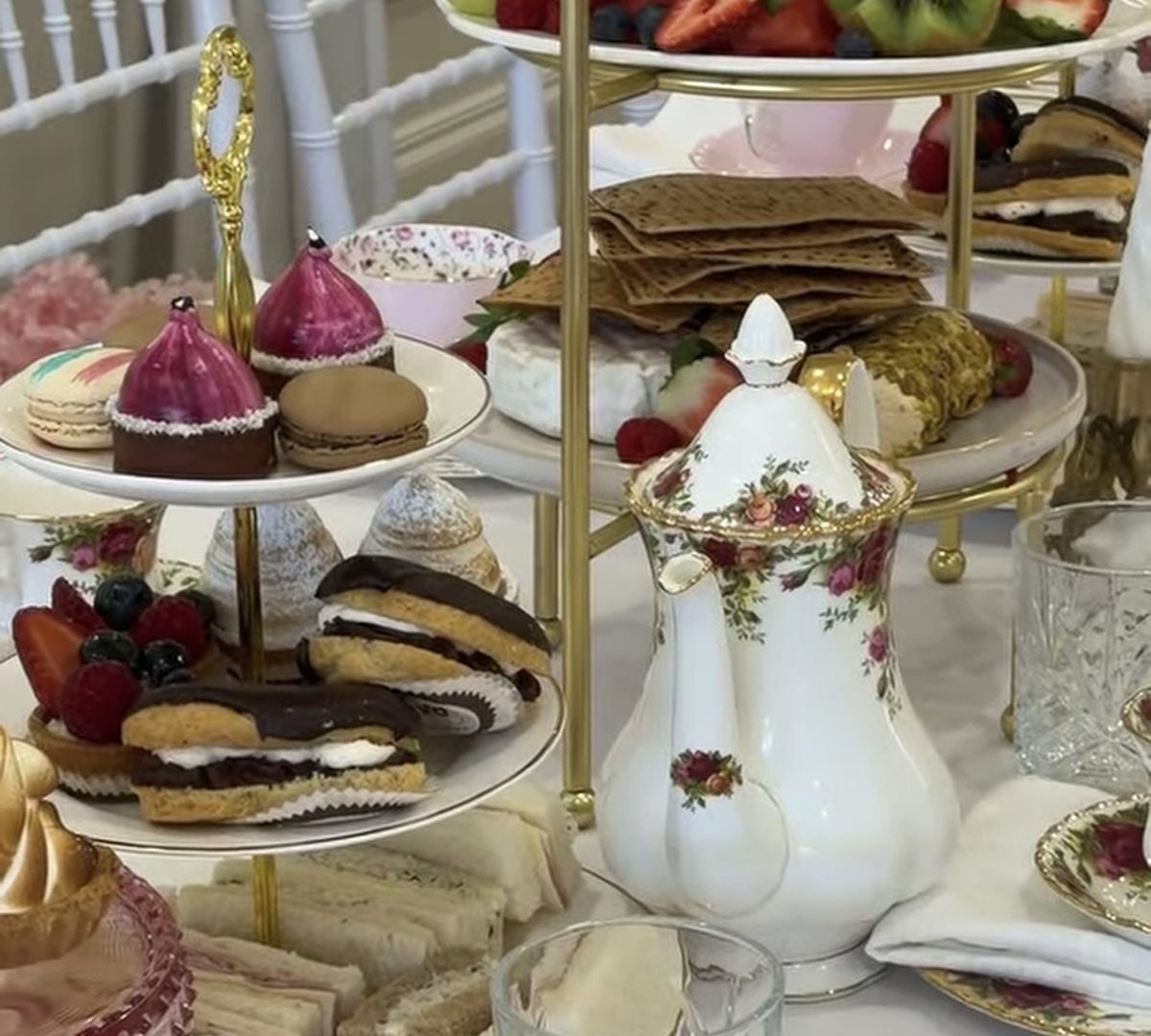 Tiered stands of cakes, sandwiches and fruit with a floral teapot and teacup